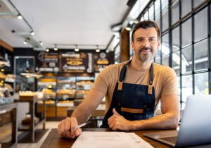A man in a shop wearing an apron smiles about his BMA payroll company